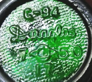 Photo of the bottom of a green glass 7-UP soda bottle from 1950, made by Owens-Illinois and marked with their Duraglas brand name. The bottle was made at their Alton, Illinois factory. 