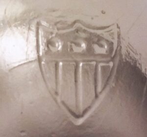 Shield / crest logo or emblem on the base of a glass jelly glass or tumbler, circa 1900-1930. Unknown glass manufacturer.