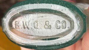 "B W O & CO" mark on base of aqua strapside flask - initials indicating B.W. O'Neil & Company, Boston, MA (c. 1882-c.1918). This was evidently a jobber, not an actual glass manufacturer.