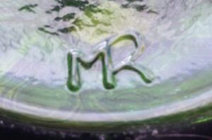 MR (letters connected) on the bottom of an olive green glass oil lamp, unknown age or origin, possibly from Europe or Mexico.