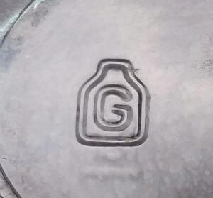 "G" inside the outline of a jar, logo mark used on the bottom of a wine bottle made by Gayner Glass Company, uncertain date. 