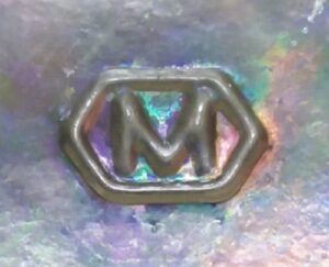 "M in a hexagon" logo, as seen on base of clear glass Pepsi bottle made in 1974. Metro Glass Bottle Company. Slight iridescence from the bottle being buried for 50 years.