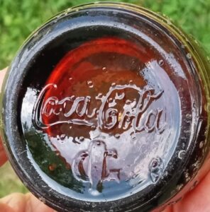 Upside down bottle superimposed over a capital "G" - logo used by Graham Glass Company, Evansville, Indiana, on bottom of amber "straight-side" type antique Coca Cola bottle.