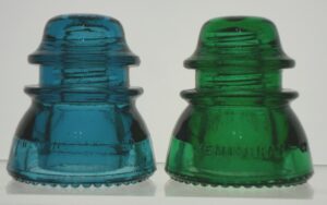 Two Hemingray-42 glass insulators, in "Hemingray Blue",  and a medium shade of true green. The green example on the right is MUCH more difficult to find and has a higher value to collectors. 