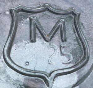 "M inside a shield" on the base of an Arrowhead brand water bottle. The "25" is a date code for 1925. (Photo courtesy of Peter Utas).