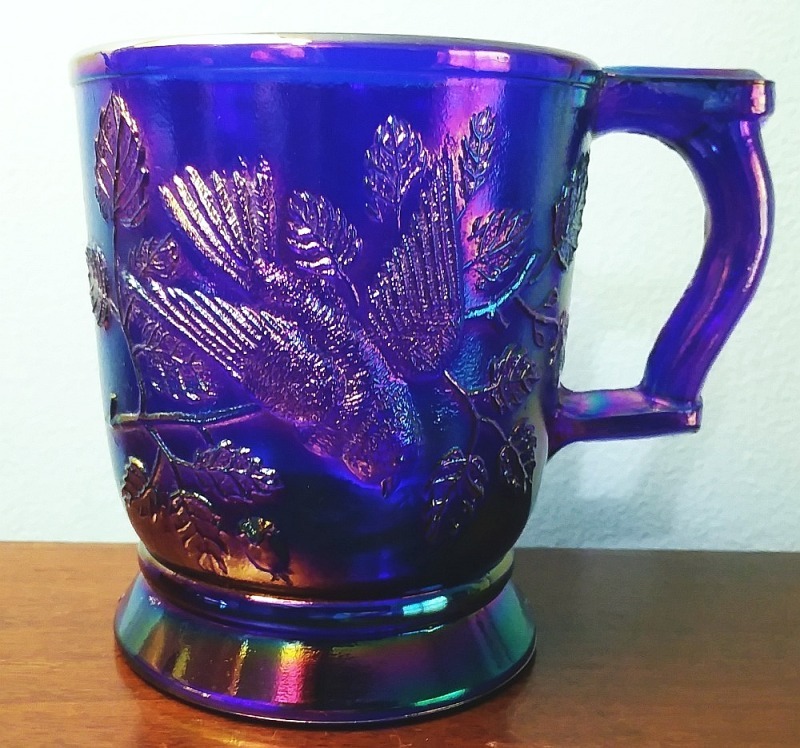 Robin in Tree" cobalt blue carnival glass mug made by Mosser Glass Company. This mug bears their "M inside the state of Ohio" mark on the inside of the base.