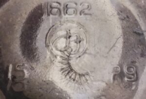 Shear mark imperfection- on base of FF Foster Forbes clear packer jar. The shear mark resembles a false eyelash.