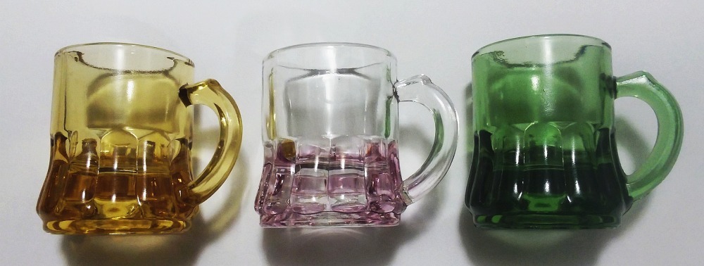 Three miniature toy mugs or "handled whisky" shotglasses in amber, light pink-amethyst and avocado green, all marked with an "F in a shield" logo on base.