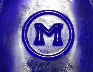 "M in a circle" trademark used by Maryland Glass Corporation, here embossed on the base of a Merrell's Milk of Magnesia cobalt blue bottle.