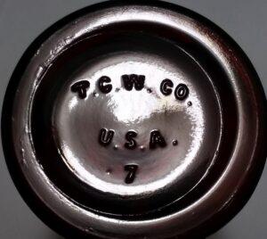 T. C. W. Co. / U.S.A. mark on base of amber glass laboratory chemical bottle made by T. C. Wheaton Company. The "7" is a mold number.