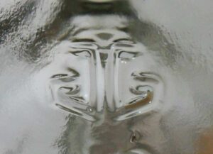 Anchor Glass Container Corporation "AG in the form of a stylized anchor"  logo, here as embossed on the base of a Jim Beam handled liquor jug, date coded 2006. This logo dates from September 1983, but has been replaced in recent years (circa 2014) by a new mark (also a stylized anchor, but which resembles a downward-pointing arrow) .