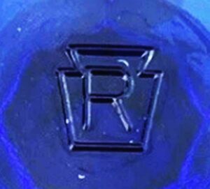 "R inside a Keystone" mark used by Rosso Wholesale Glass Dealers, Inc. Here as seen on base of cobalt blue eyewash cup. (Photo courtesy of eBay seller "deep_south_general_store")
