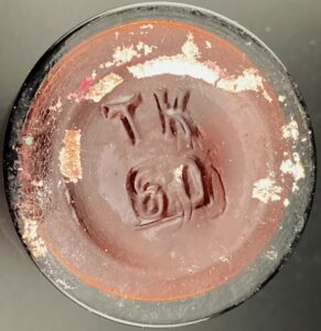 "T K" on base of amber anesthesia bottle. The "60" probably indicates capacity in milliliters. (Photo courtesy of June Bergeron).