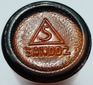 "S inside a triangle" over SANDOZ - on base of small amber pharmaceutical bottle