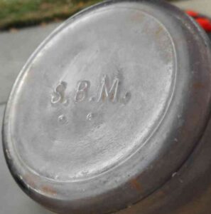 "S.B.M." mark on the base of a light amethyst, mouthblown (handmade) cylindrical liquor bottle with tooled "brandy" type lip.  So far unknown, several bottles (and base shards) have been found over the years, all found in the Western states of the United States. This mark is probably the initials of an unidentified distiller, beverage distributor or glass factory. (Photo courtesy of E. Rex)