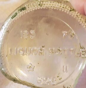 Base of clear liquor bottle made by Star City Glass Company. This bottle would probably be from the Coventry, Rhode Island plant. The piece bears the diagnostic "123" liquor bottle permit code number, and a date code for 1973. The "C" is not clearly shown inside the star. (Photo courtesy of Jodi Gerstenhaber).
